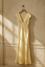 Butter yellow silk column maxi dress, hanging on wooden hanger against plaster wall