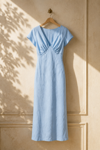 Light blue linen column maxi dress, hanging on wooden hanger against plaster wall