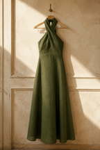 Olive green linen a-line maxi dress, hanging on wooden hanger against plaster wall