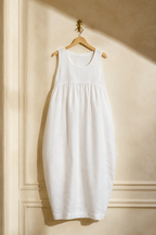 White linen cocoon maxi dress, hanging on wooden hanger against plaster wall