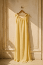 Butter yellow linen shift maxi dress, hanging on wooden hanger against plaster wall