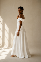 White linen a-line maxi dress, three-quarter view, ruffled neckline, fitted bodice, flowing A-line
