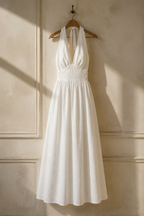 White linen a-line maxi dress, hanging on wooden hanger against plaster wall