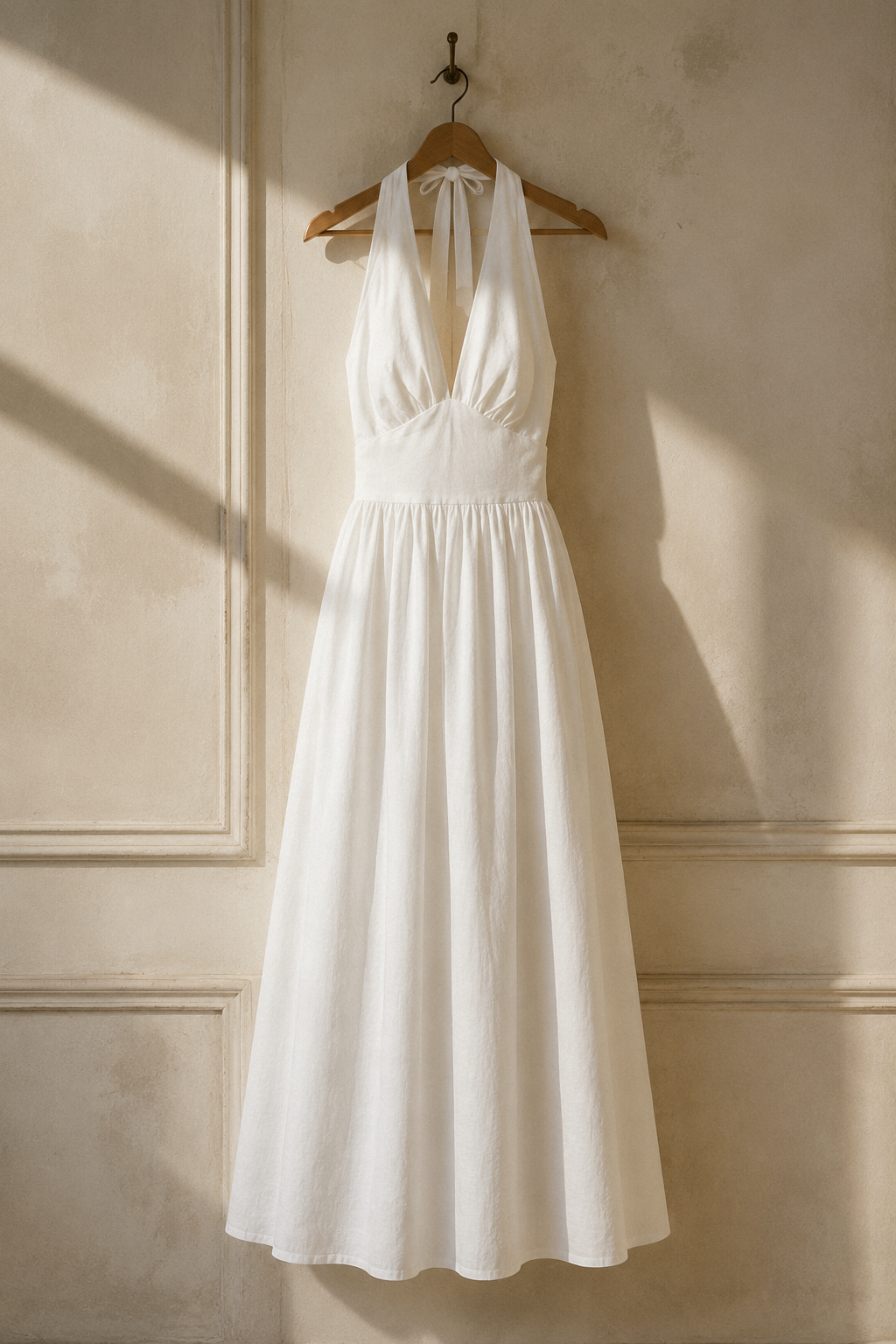 White linen a-line maxi dress, hanging on wooden hanger against plaster wall