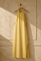 Butter yellow linen shift maxi dress, hanging on wooden hanger against plaster wall