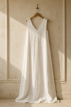Ivory linen shift maxi dress, hanging on wooden hanger against plaster wall
