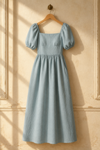 Light blue linen a-line maxi dress, hanging on wooden hanger against plaster wall