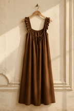 Brown linen a-line maxi dress, hanging on wooden hanger against plaster wall