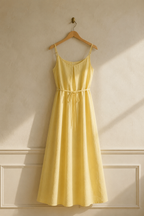 Butter yellow linen slip maxi dress, hanging on wooden hanger against plaster wall