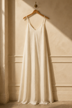 Ivory linen slip maxi dress, hanging on wooden hanger against plaster wall