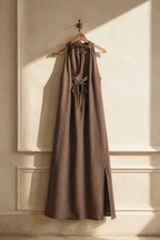 Brown linen shift maxi dress, hanging on wooden hanger against plaster wall