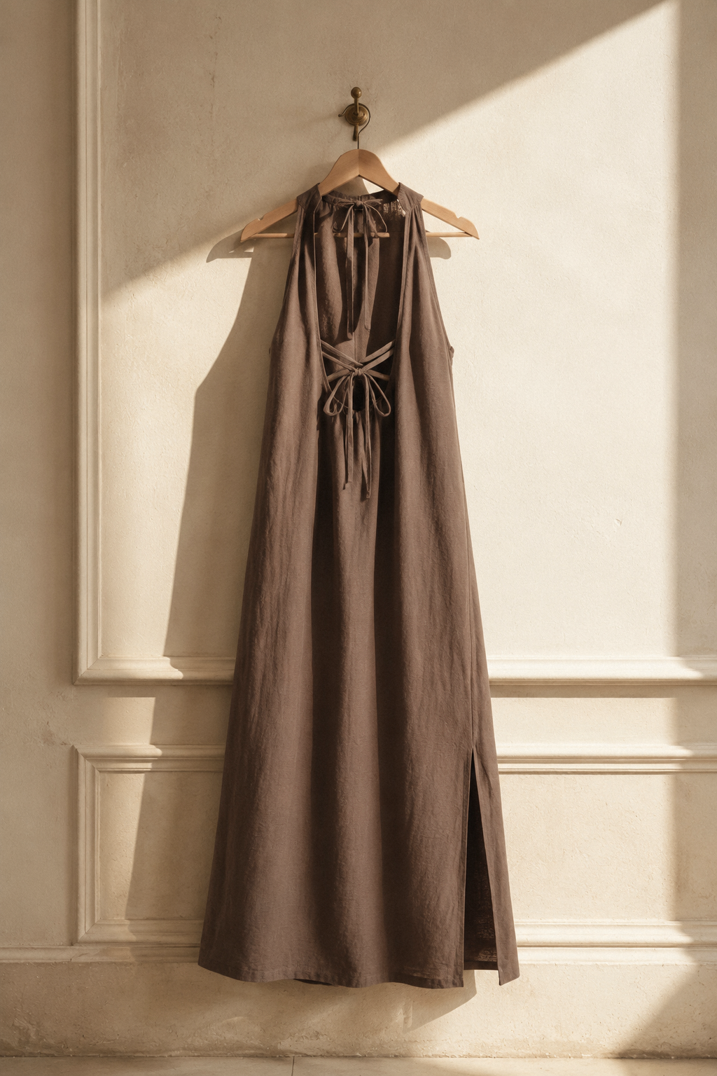 Brown linen shift maxi dress, hanging on wooden hanger against plaster wall