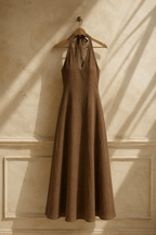 Brown linen a-line maxi dress, hanging on wooden hanger against plaster wall