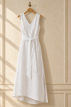 White linen wrap maxi dress, hanging on wooden hanger against plaster wall