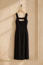 Black linen column midi dress, hanging on wooden hanger against plaster wall