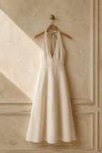 Ivory linen a-line midi dress, hanging on wooden hanger against plaster wall