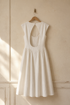 Ivory linen a-line midi dress, hanging on wooden hanger against plaster wall