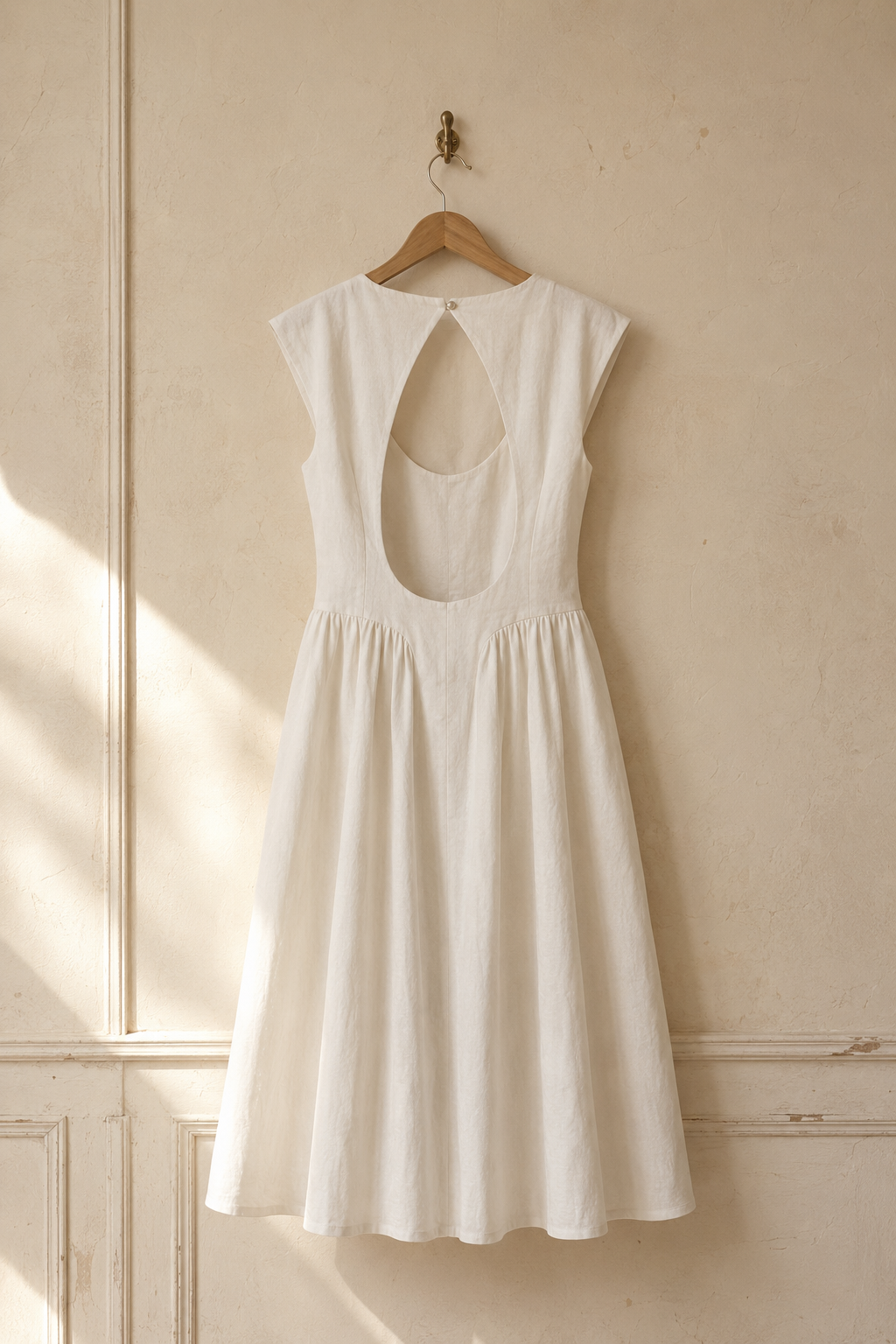 Ivory linen a-line midi dress, hanging on wooden hanger against plaster wall
