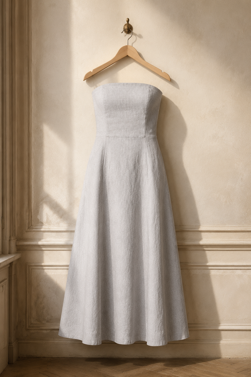 Light grey linen a-line midi dress, hanging on wooden hanger against plaster wall