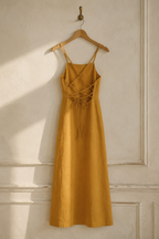Mustard yellow linen a-line midi dress, hanging on wooden hanger against plaster wall