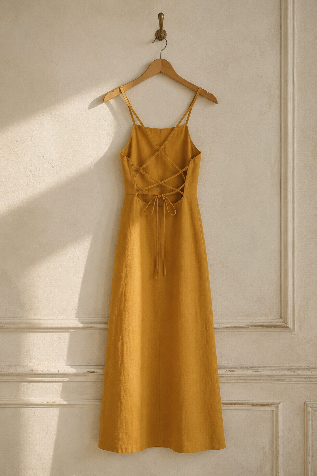 Mustard yellow linen a-line midi dress, hanging on wooden hanger against plaster wall