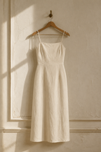 Ivory linen column midi dress, hanging on wooden hanger against plaster wall