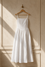 White linen a-line midi dress, hanging on wooden hanger against plaster wall