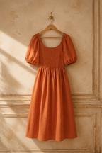 Rust orange linen a-line midi dress, hanging on wooden hanger against plaster wall