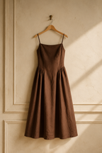 Brown linen a-line midi dress, hanging on wooden hanger against plaster wall