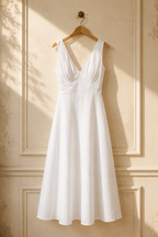 White linen a-line midi dress, hanging on wooden hanger against plaster wall