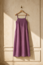 Purple linen slip midi dress, hanging on wooden hanger against plaster wall