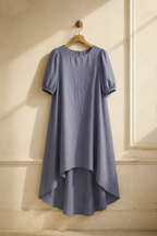 Blue-grey linen shift midi dress, hanging on wooden hanger against plaster wall