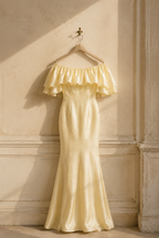 Butter yellow silk column midi dress, hanging on wooden hanger against plaster wall