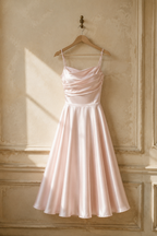 Light pink silk a-line midi dress, hanging on wooden hanger against plaster wall