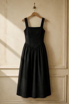 Black linen a-line midi dress, hanging on wooden hanger against plaster wall