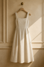 Ivory linen a-line midi dress, hanging on wooden hanger against plaster wall