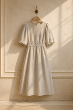 Beige linen a-line midi dress, hanging on wooden hanger against plaster wall