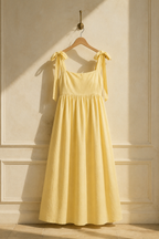 Butter yellow linen a-line midi dress, hanging on wooden hanger against plaster wall
