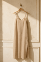 Beige linen slip midi dress, hanging on wooden hanger against plaster wall