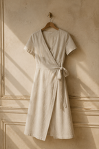 Oatmeal linen wrap midi dress, hanging on wooden hanger against plaster wall