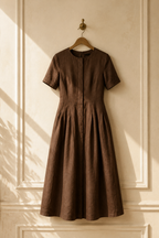 Brown linen a-line midi dress, hanging on wooden hanger against plaster wall