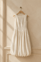 Ivory linen a-line midi dress, hanging on wooden hanger against plaster wall