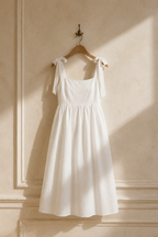 White linen a-line midi dress, hanging on wooden hanger against plaster wall