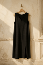 Black cotton shift midi dress, hanging on wooden hanger against plaster wall