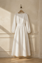White linen a-line midi dress, hanging on wooden hanger against plaster wall