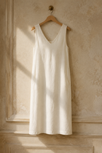 Ivory linen shift midi dress, hanging on wooden hanger against plaster wall