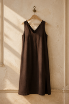 Dark brown linen shift midi dress, hanging on wooden hanger against plaster wall