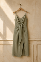 Sage green linen wrap midi dress, hanging on wooden hanger against plaster wall