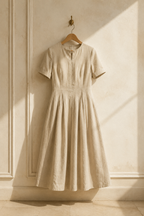Beige linen a-line midi dress, hanging on wooden hanger against plaster wall