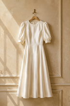 Ivory silk a-line midi dress, hanging on wooden hanger against plaster wall